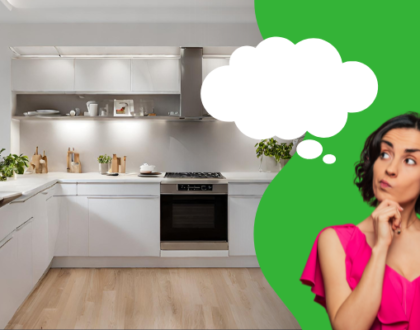 A modern, spacious kitchen with white cabinetry, stainless steel appliances, and light wooden flooring. On the right, a woman in a bright pink top appears deep in thought, with a contemplative expression and her hand on her chin. A large thought bubble emanates from her head, suggesting she is dreaming or considering ideas for home renovations, rebuilds, or remodels.