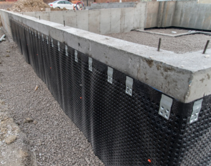 A foundation wall with waterproofing membrane installed on the exterior, showing the dimpled drainage board applied to the concrete and anchored in place